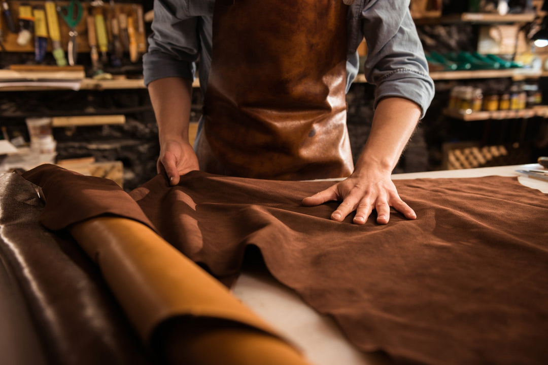Brown full-grain leather hide being inspected by hand on a workbench, highlighting material craftsmanship and quality associated with an elegant chic style by Dylan Archer.